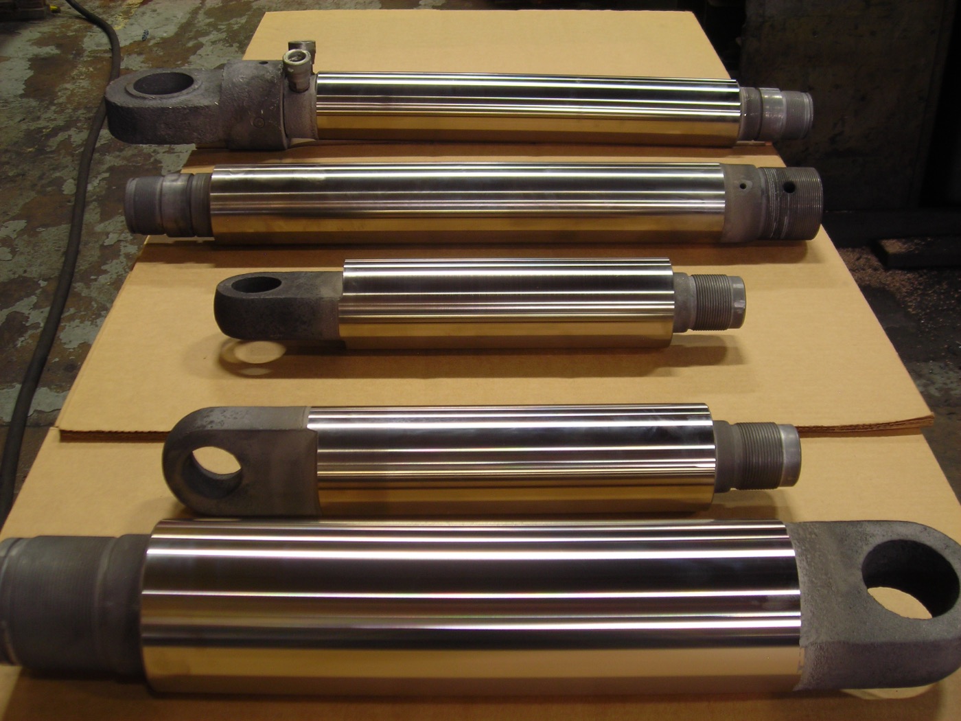 Five reconditioned hydraulic mining cylinder rods, ground and polished, laid out in the shop